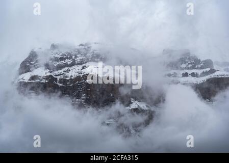 Scharfe Berggipfel teilweise mit Schnee umgeben von nebligen bedeckt Nebel unter bewölktem Himmel im Winter Stockfoto