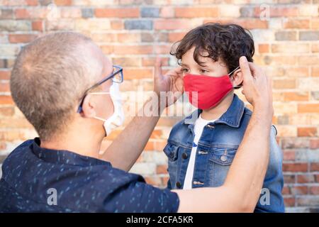 Mann trägt eine Schutzmaske und setzt eine Gesichtsmaske auf einen Sohn auf der Straße. Konzept der Sicherheit während des Covid-19-Ausbruchs. Stockfoto