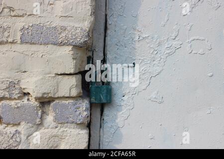 Sicherheits-Vorhängeschloss aus schwerem Metall Tür in weiß lackiert und Weiße Backsteinmauer Stockfoto