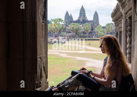 Seitenansicht einer konzentrierten jungen Frau mit Kamera, die einen alten religiösen Tempel betrachtete, während sie sich in Angkor Wat in Kambodscha ausruhte Stockfoto