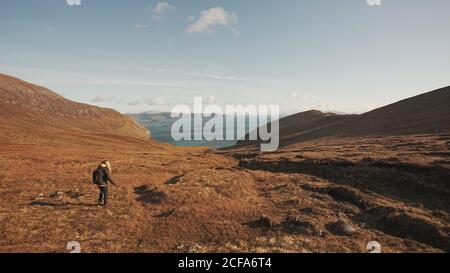 Rückansicht einer nicht erkennbaren Frau, die auf einer wunderschönen Naturlandschaft und einem Meer unterwegs ist, während sie auf einer Klippe in Irland steht und wegschaut Stockfoto