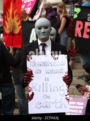 Ein maskierter Protestler, mit gefälschtem Blut bedeckte Hände, hält während eines Extinction Rebellion Protestes ein Plakat vor der Bank of England in der City of London. Stockfoto