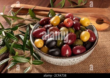 Oliven. Eine Vielzahl von grünen, schwarzen und roten Oliven, eine Nahaufnahme mit Blättern auf einem rustikalen Holzhintergrund Stockfoto