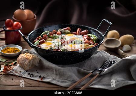 Pfanne mit Spiegelei mit traditionellen spanischen Chorizo Würstchen und Grüne Paprika serviert auf rustikalem Holztisch mit Küchenutensilien Und Produkte Stockfoto
