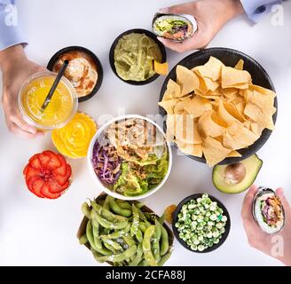 Draufsicht der Ernte anonyme Menschen essen verschiedene Arten von Traditionelle spanische Tapas, darunter Nachos mit Guacamole und gekochte Sojabohnen Edamame und Salate während der Party Stockfoto