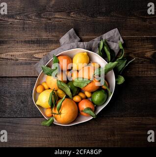 Draufsicht auf reife Orangen und Mandarinen in Schale gelegt Mit Kumquat und Zitrone auf Holztisch mit Serviette Stockfoto