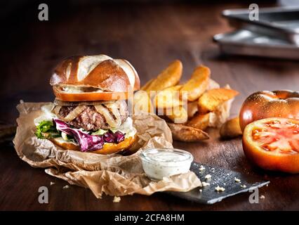 Appetitlich großen Burger mit frischem Gemüse und Rindfleisch Patty mit Gebratene Kartoffeln auf Schiefertafel mit Pommes serviert Stockfoto