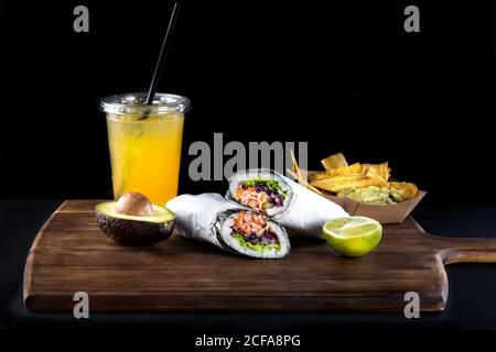 Set von typischen mexikanischen Snacks einschließlich gebratener Kochbananen mit Guacamole Und Sushi Burritos serviert mit traditionellen kalten Obst Soda gegen Schwarzer Hintergrund Stockfoto
