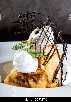Exquisit servierte Portion süßer Biskuitkuchen mit Vanilleeis Creme und Schokolade dekoratives Gitter Stockfoto