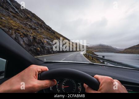 Von innen eine Autoansicht einer anonymen Person, die einen fährt Auto in einem regnerischen Tag mit einem verschneiten Berg Hintergrund Stockfoto