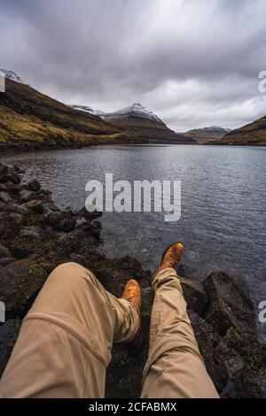 Nicht erkennbare Person, die in der Nähe des Sees sitzt und Beine zeigt, die in Färöer entspannen Insel Stockfoto