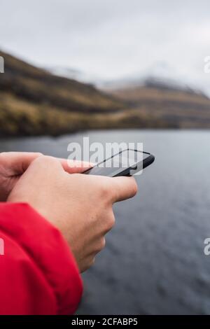 Anonymer Mann mit Smartphone in der Nähe eines Sees auf der Färöer-Insel Stockfoto