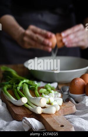 In einer Schüssel zerbrechende Hände einer Frau, in der sich frische Frühlingszwiebeln und Pilze auf dem Schneidebrett in der Nähe von Mohnsamen befinden Stockfoto