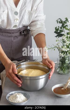 Nicht erkennbare weibliche in grauen Schürze Putting Bowl mit frischem Teig Auf dem Tisch neben Mehl und Apfelmus während der Zubereitung von Gebäck Stockfoto