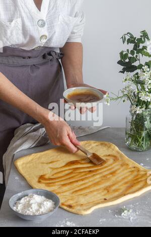 Nicht erkennbare Dame in Schürze Verbreitung von frischem Apfelmus weich Teig beim Zubereiten von Teig in der Nähe von Mehl und Blumenstrauß Stockfoto