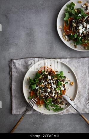 Blick von oben auf Teller mit leckeren gebackenen Süßkartoffelsalat Und Besteck auf grauen Tisch während des Mittagessens gelegt Stockfoto