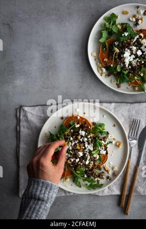 Overhead anonyme Person Zugabe von Zutaten zu leckeren gebackenen Süßkartoffeln Salat während der Zubereitung des Mittagessens über einem grauen Tisch Stockfoto