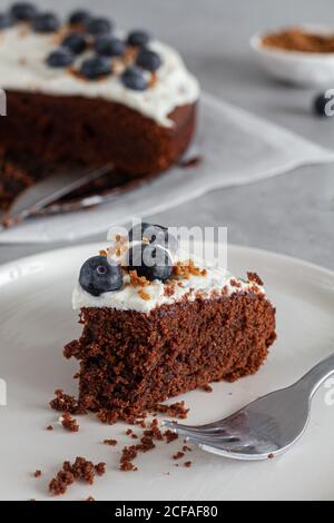 Ein Stück hausgemachter Schokoladenkuchen mit frischem Schlagsahne Sahne und ganze Heidelbeeren auf dem Tisch in der hellen Küche platziert Stockfoto