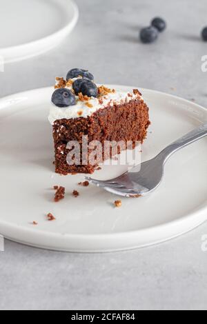Ein Stück hausgemachter Schokoladenkuchen mit frischem Schlagsahne Sahne und ganze Heidelbeeren auf dem Tisch in der hellen Küche platziert Stockfoto