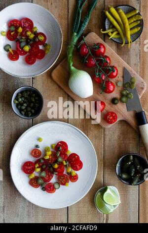 Draufsicht auf Teller mit Salat aus frischer Kirsche Tomaten und eingelegte Gurken mit Paprika und Frühlingszwiebel und Platziert auf Holztisch neben gequetschten Kalk Stockfoto