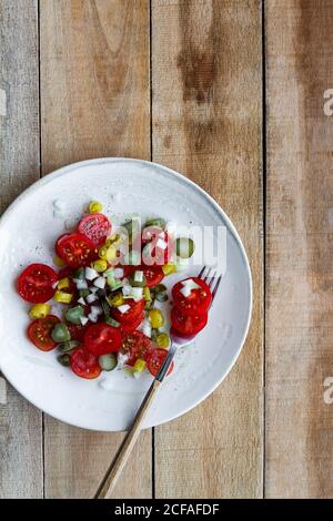 Draufsicht auf Teller mit Salat aus frischer Kirsche Tomaten und eingelegte Gurken mit Paprika und Frühlingszwiebel und Platziert auf Holztisch neben gequetschten Kalk Stockfoto
