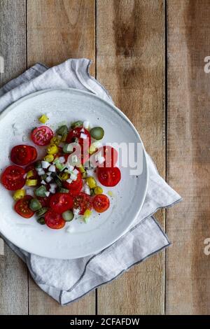 Draufsicht auf Teller mit Salat aus frischer Kirsche Tomaten und eingelegte Gurken mit Paprika und Frühlingszwiebel und Platziert auf Holztisch neben gequetschten Kalk Stockfoto