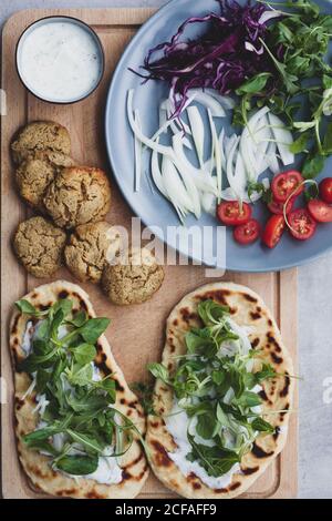 Von oben der Lebensmittelzusammensetzung Falafel und frisches Gemüse auf Brot in der Nähe mit Salat auf Schneidebrett Stockfoto