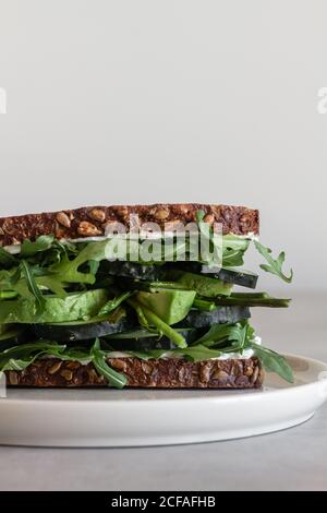 Nahaufnahme von köstlichen natürlichen Sandwich mit Vollkorntoastbrot gemacht Mit frischen grünen Kräutern mit Gurke und Avocado serviert Weiße Platte vor weißem Hintergrund Stockfoto