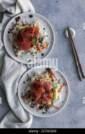 Von oben schmackhaft appetitlich geschnittener Lachs auf weißem Reis mit Gemüse auf dem Teller und Holzstäbchen auf dem Tisch Stockfoto