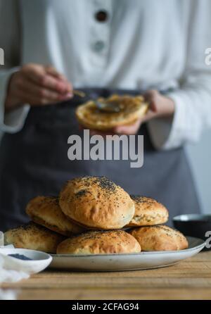 Teller mit frischen Mohnbrötchen auf Holztisch gelegt Fast anonymer Koch schmiert frisches Gebäck mit Marmelade Stockfoto
