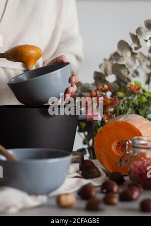 Crop kochen mit Suppenschüssel und Löffel in den Händen Kochen Kürbis- und Kastaniensahnesuppe Stockfoto