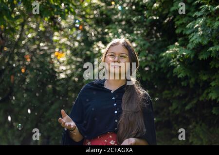 Nahaufnahme Bild von einem präteen Mädchen mit langen braunen Haaren und Seifenblasen. Grüne Blätter im Hintergrund Stockfoto