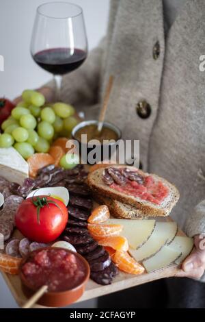 Gesichtsloser Kellner, der ein Holztablett mit Fleischgemüse trägt Früchte und ein Glas Rotwein Stockfoto
