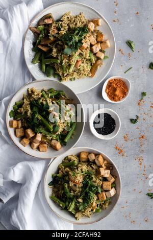 Von oben schmackhafte gekochte Gericht mit Reis und grünen Bohnen Servieren auf Tellern mit Gewürzen auf dem Tisch Stockfoto
