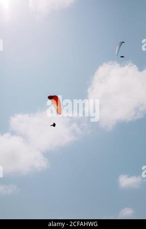 Von unten fliegen Menschen mit bunten Gleitschirmen in bewölktem Himmel In der Nähe der Durdle Door am Tag Stockfoto