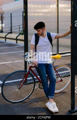 Nachdenklicher Mann, der zur Sonnenuntergangszeit auf seinem Fahrrad auf einem Parkplatz steht. Stockfoto