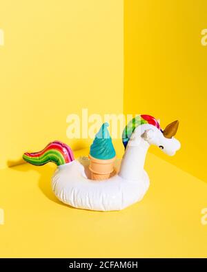 High Angle Komposition mit aufblasbarem Einhorn Spielzeug und künstlichem Eis Creme Kegel vor gelbem Hintergrund platziert Stockfoto