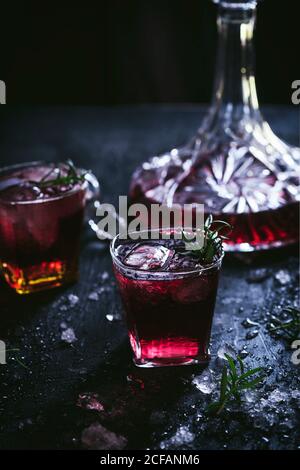 Karaffe und Kristallgläser mit Eis gefüllt mit Rotwein Auf schwarzem Tisch Stockfoto