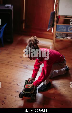 Von oben Seitenansicht des ethnischen Kindes in legerer Kleidung Sitzen auf Holzboden und spielen mit Spielzeugauto an Zu Hause Stockfoto