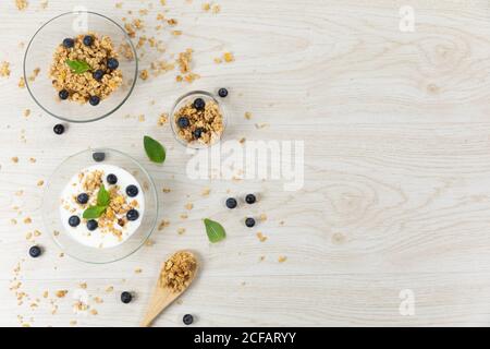 Blick auf drei Schalen mit Müsli, Nüssen, Heidelbeeren und Joghurt auf weißer Holzfläche Stockfoto