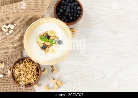 Blick auf drei Schalen mit Müsli, Nüssen, Heidelbeeren und Joghurt auf weißer Holzfläche Stockfoto