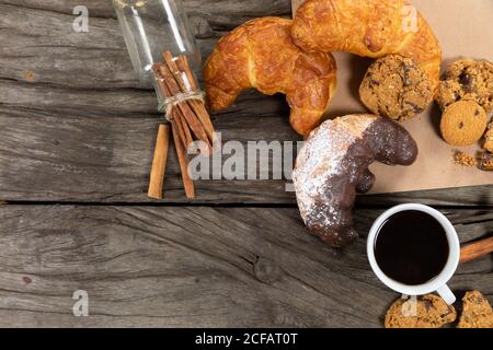 Blick auf Cookies, Brezeln und Croissants auf einem Tischtuch mit einer Tasse Kaffee auf Holzoberfläche gelegt Stockfoto