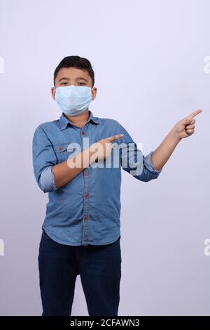 Indische niedlich junge weraing chirurgische Maske zeigt Finger in Richtung seiner linken Seite. Stockfoto