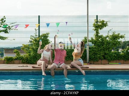 Eine Gruppe von Freunden, die eine Poolparty machen, während sie tanzen, lachen und Cocktails trinken Stockfoto