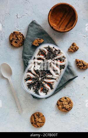 Blick von oben auf Haferflocken Cookies Plastikbehälter mit Eis Platziert auf Serviette neben Löffel und Schüssel auf Stuckoberfläche Stockfoto
