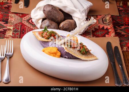 Wolfsbarschfilet mit violettem Kartoffelpüree, Karottenpüree und Tomatensalsa. Stockfoto