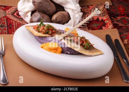 Wolfsbarschfilet mit violettem Kartoffelpüree, Karottenpüree und Tomatensalsa. Stockfoto