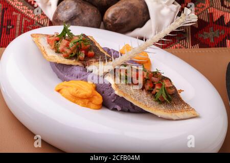 Wolfsbarschfilet mit violettem Kartoffelpüree, Karottenpüree und Tomatensalsa. Stockfoto