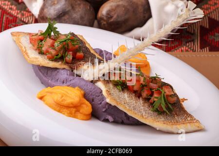 Wolfsbarschfilet mit violettem Kartoffelpüree, Karottenpüree und Tomatensalsa. Stockfoto