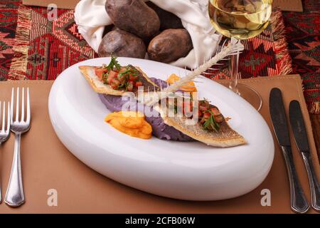 Wolfsbarschfilet mit violettem Kartoffelpüree, Karottenpüree und Tomatensalsa. Stockfoto